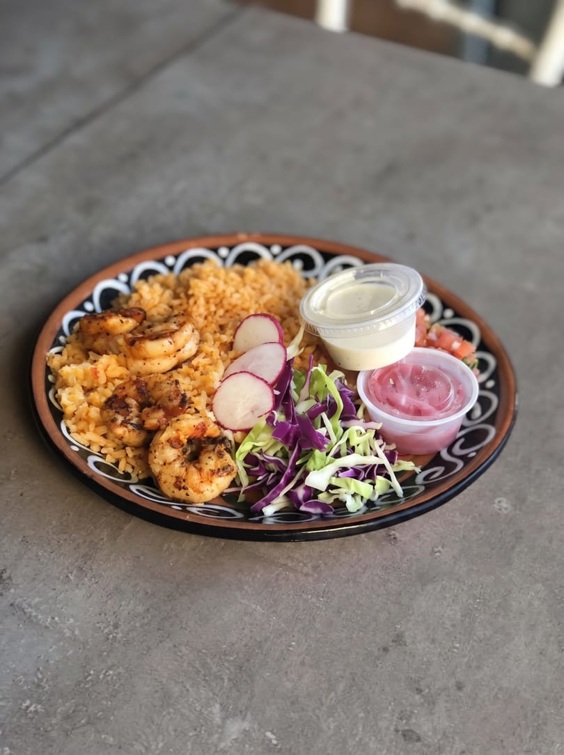 Shrimp and rice dish with sliced radishes, shredded cabbage, and small containers of sauces.