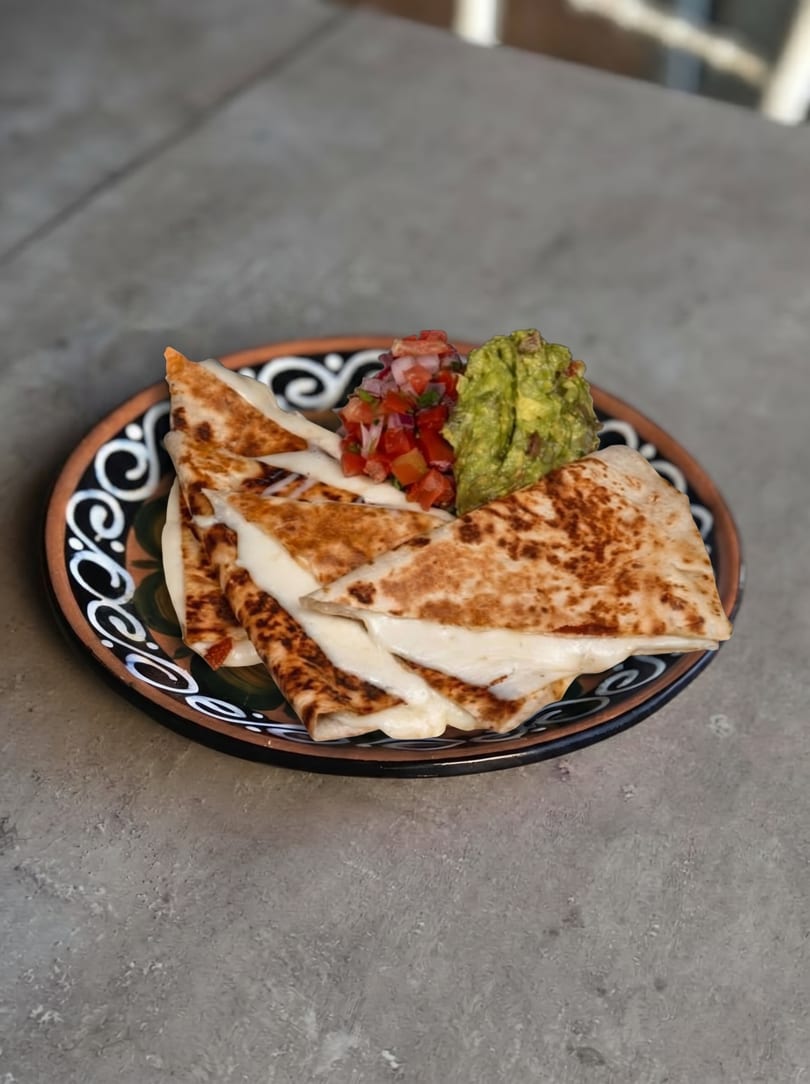 Cheese quesadillas with pico de gallo and guacamole on a decorative plate.