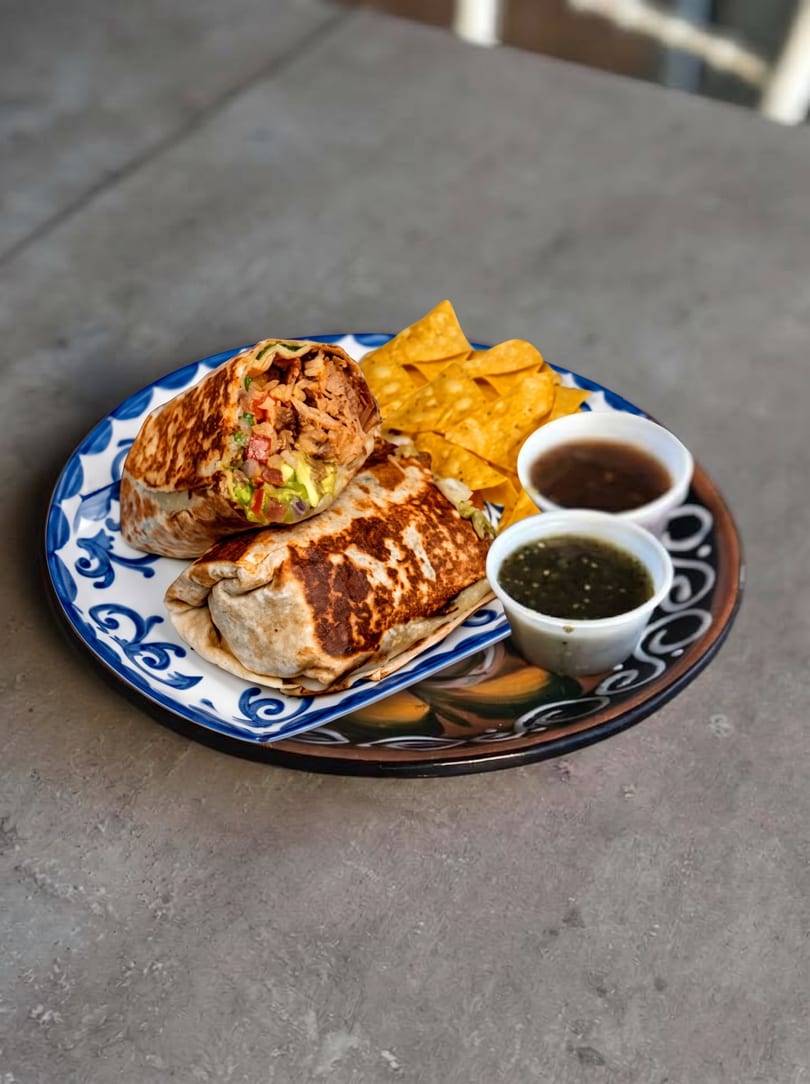 Two burritos, tortilla chips, and two small cups of salsa on a decorative blue and white plate.
