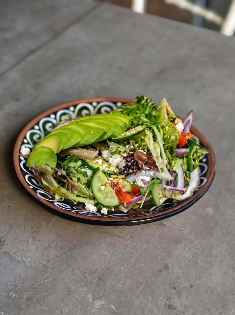 Colorful salad with avocado, mixed greens, cucumber, red onion, and feta cheese on a decorative plate.